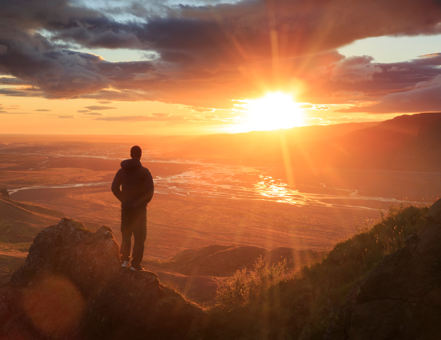Hero image showing man looking at sunset from mountain cliff